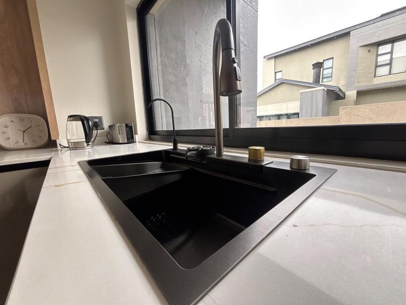 Modern kitchen featuring a sleek black undermount sink, high-arc gooseneck faucet, and premium stone countertops set against a large window.