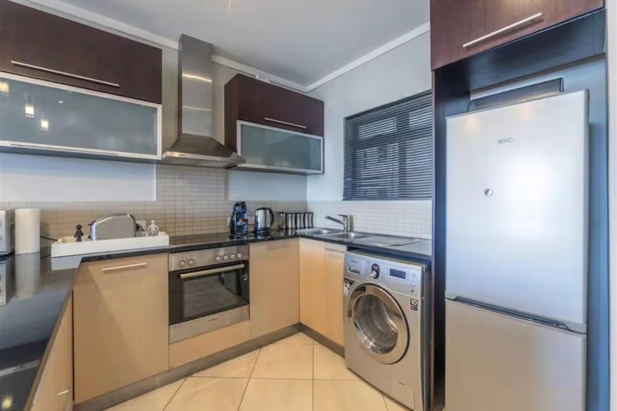 A functional kitchen featuring modern cabinetry, stainless steel appliances including an oven and extractor fan, tiled backsplash, and integrated laundry plumbing.
