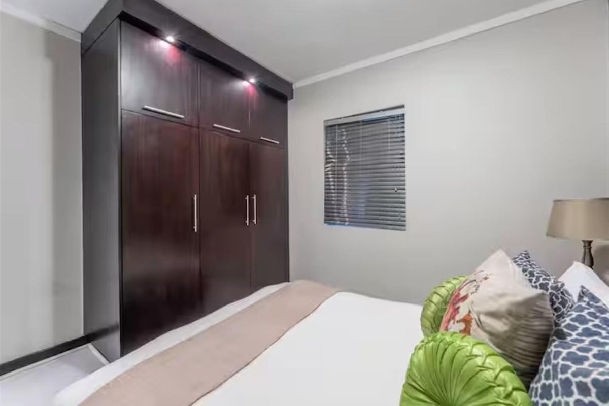 A well-maintained bedroom featuring dark wood built-in wardrobes with integrated lighting and venetian blinds.