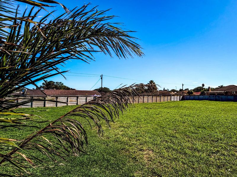 A view of a vacant residential plot featuring a well-maintained grass lawn and perimeter boundary walling.