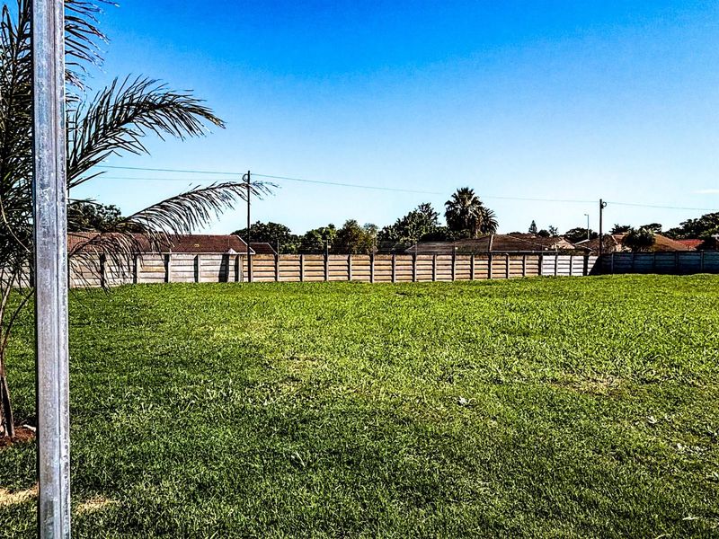 A level, grassed residential vacant stand enclosed by perimeter fencing, offering a clear space ready for development.