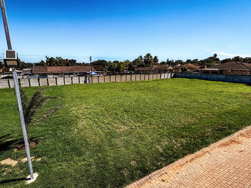 A spacious, level residential vacant plot featuring well-maintained lawn, perimeter concrete walling, and paved driveway access.