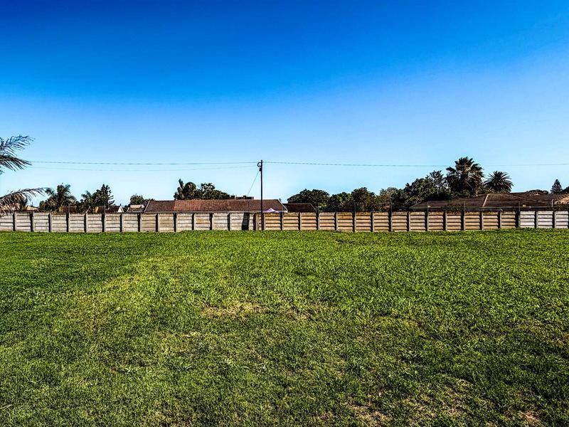 A spacious, level vacant residential plot featuring a well-maintained grass lawn and a secure perimeter boundary wall.
