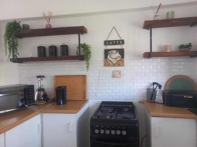 A compact kitchen featuring white subway tile backsplash, wooden countertops, open shelving, and a freestanding black stove.
