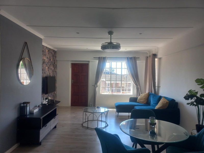 Open plan living and dining area featuring laminate flooring, a feature stone-cladding wall, and a ceiling fan.