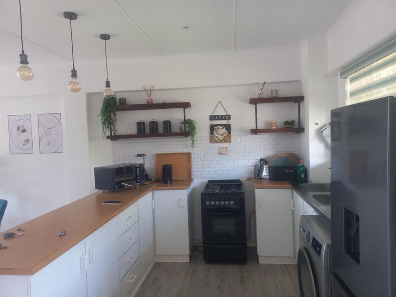 A functional kitchen featuring white cabinetry, wooden countertops, a subway tile backsplash, open shelving, and integrated space for laundry appliances.