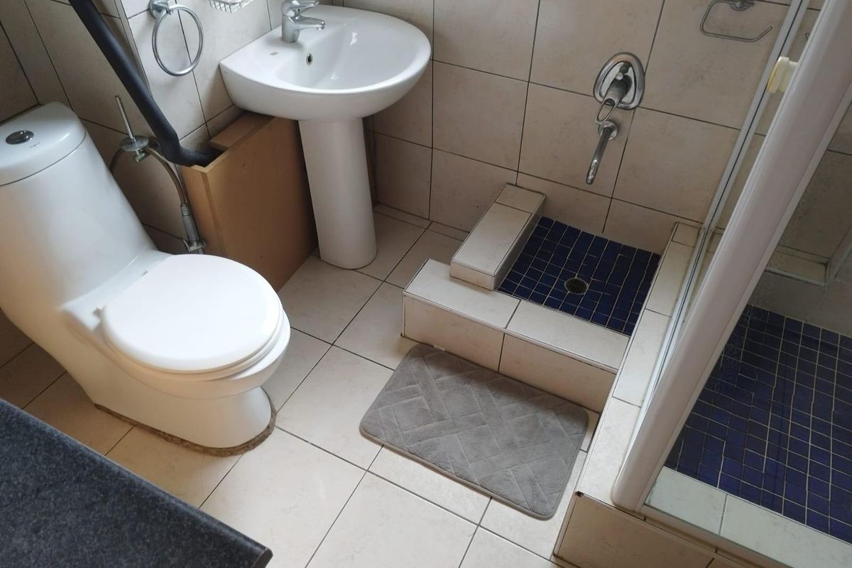 A functional bathroom featuring a pedestal basin, toilet, and a tiled shower enclosure with a raised step entry.