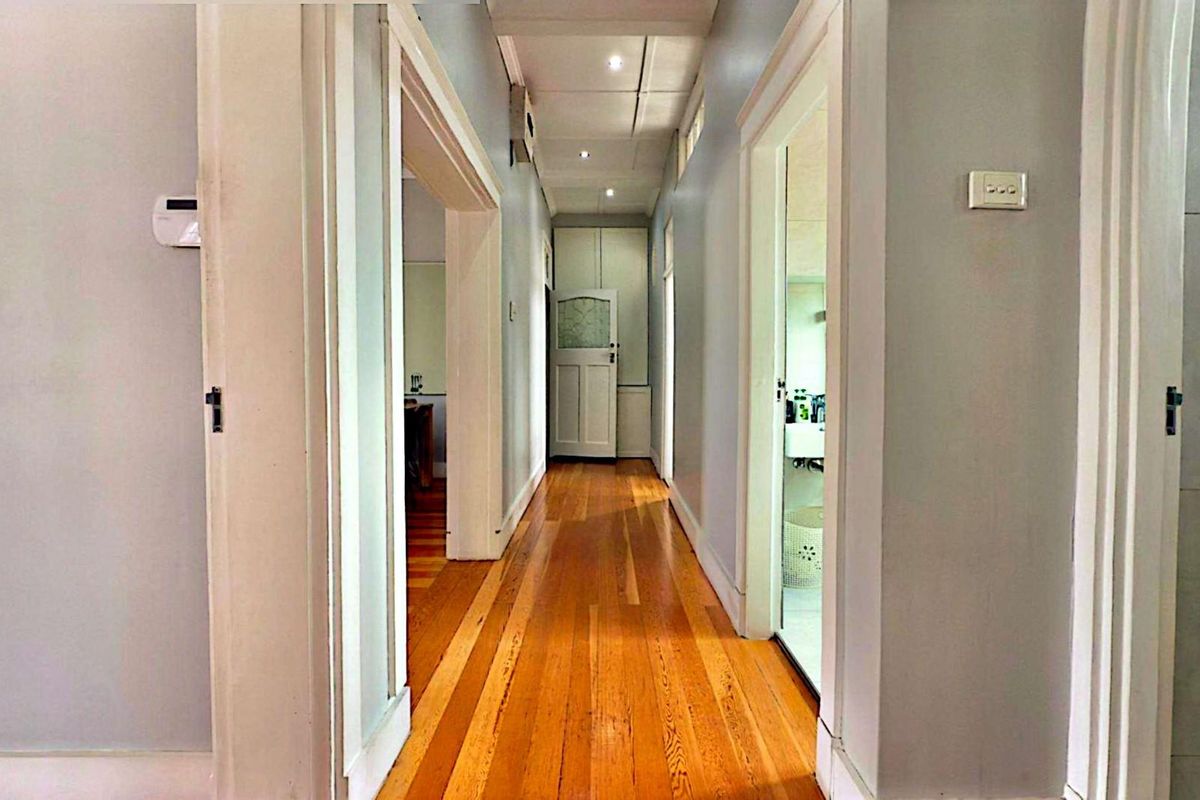 A bright hallway featuring polished timber flooring, recessed downlighting, and access to multiple rooms throughout the apartment.