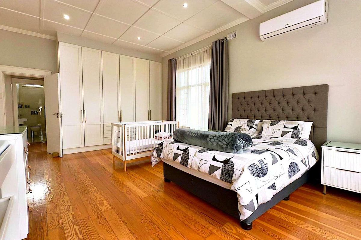 Spacious bedroom featuring polished timber flooring, extensive built-in cabinetry, recessed ceiling lighting, and a wall-mounted air conditioning unit.
