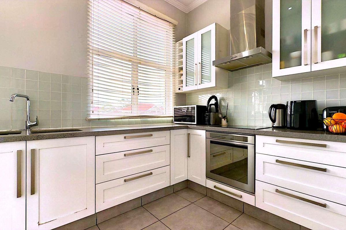 A well-maintained kitchen featuring white cabinetry, stone-look countertops, a built-in oven, stainless steel extractor fan, and a tiled backsplash.