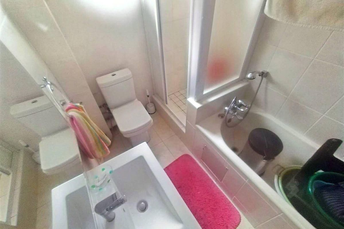 A functional bathroom featuring a built-in bathtub, separate shower enclosure, toilet, and a wall-mounted vanity basin with tiled walls.