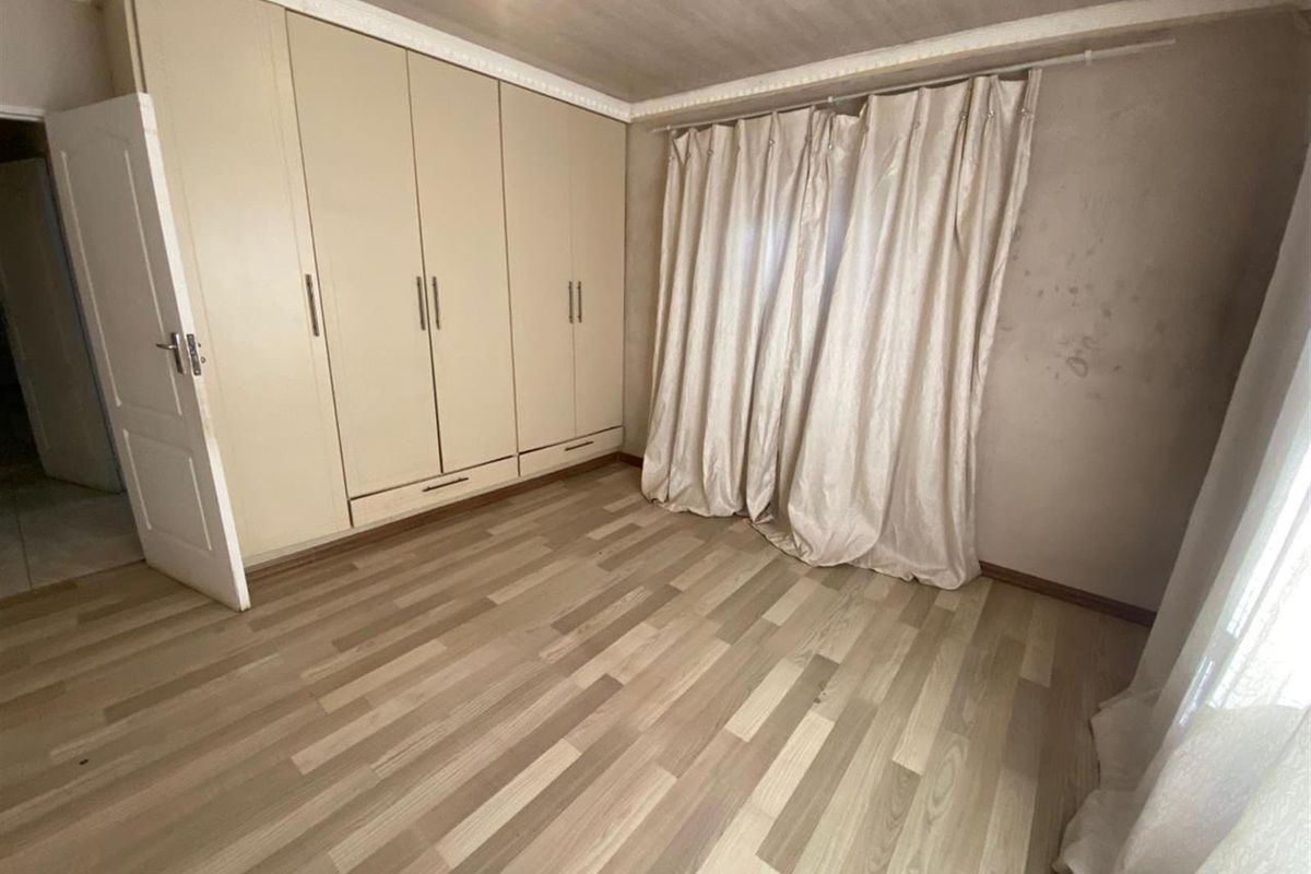 An empty bedroom featuring built-in cupboards, laminate flooring, and decorative cornice. The walls show visible signs of staining and surface wear.