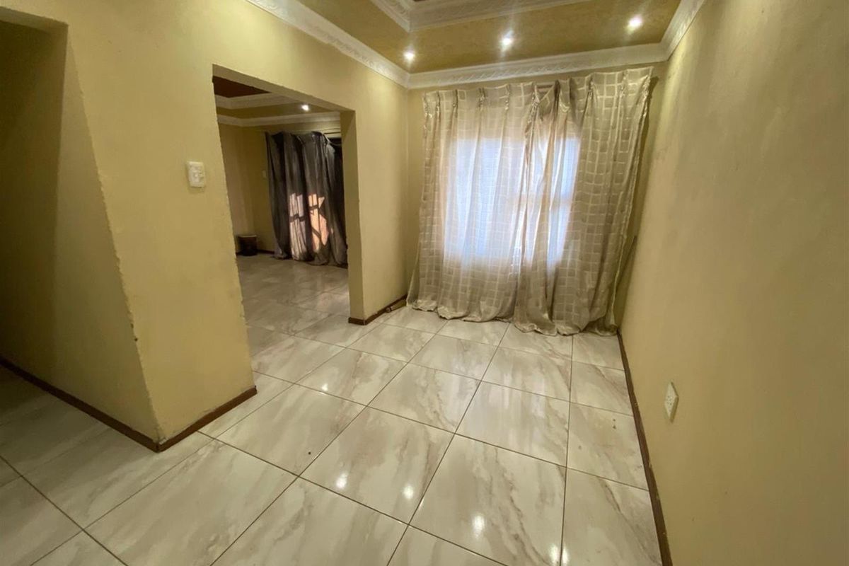 An empty living room featuring polished porcelain floor tiles, a recessed ceiling with downlights, and decorative coving.