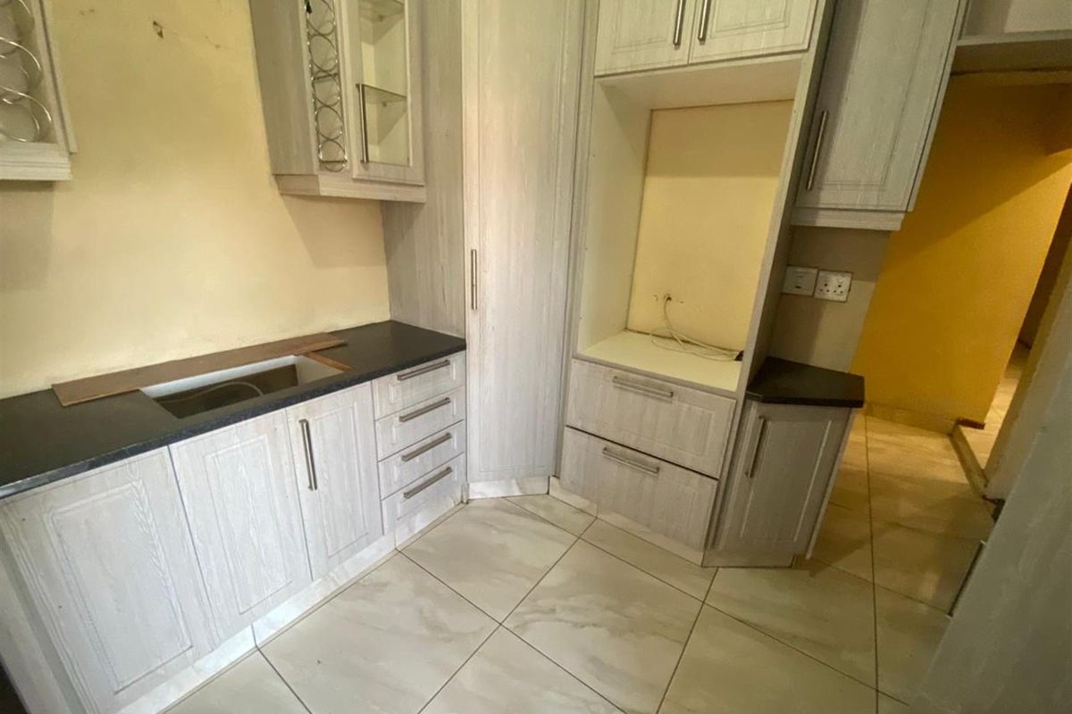 A vacant kitchen area featuring built-in cabinetry, tiled flooring, and dedicated appliance housing, currently requiring minor repairs and cosmetic updates.