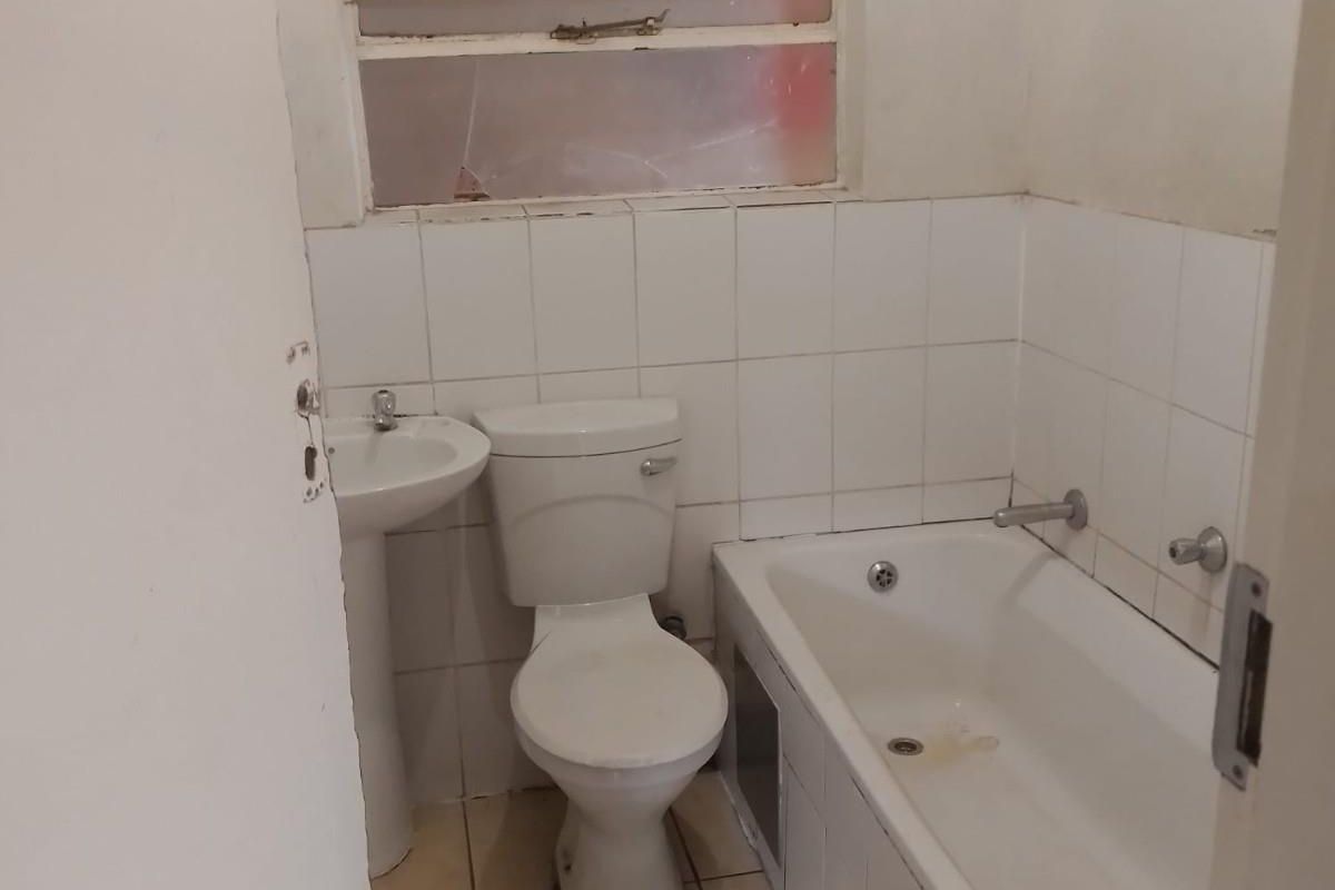 A compact bathroom featuring a standard bathtub, pedestal basin, and toilet, finished with white wall tiles and floor tiling.