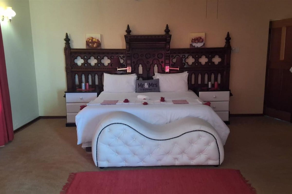A spacious bedroom featuring a large, ornate wooden headboard and integrated bedside cabinetry, providing a classic aesthetic.