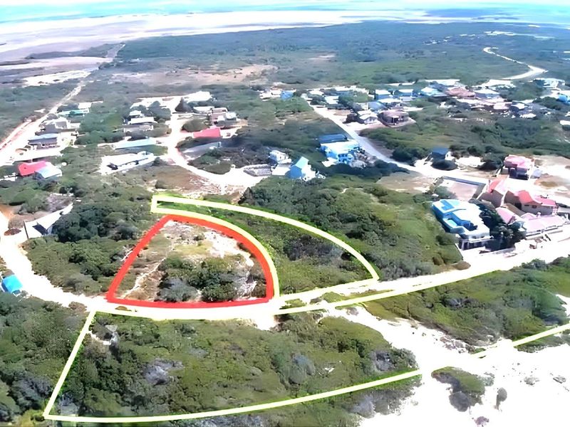 An aerial view of a vacant residential plot highlighted in red, situated within a coastal neighborhood with surrounding natural vegetation.