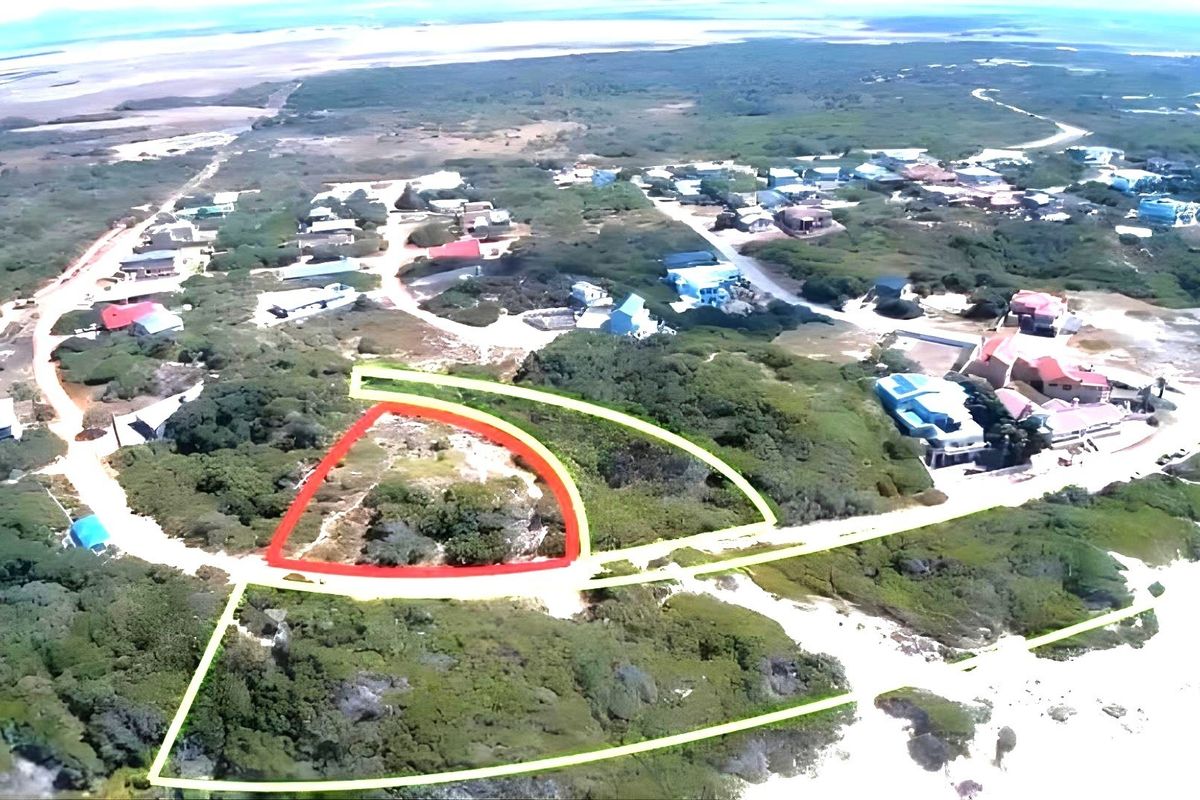 An aerial view of a vacant residential plot highlighted in red, situated within a coastal neighborhood with surrounding natural vegetation.
