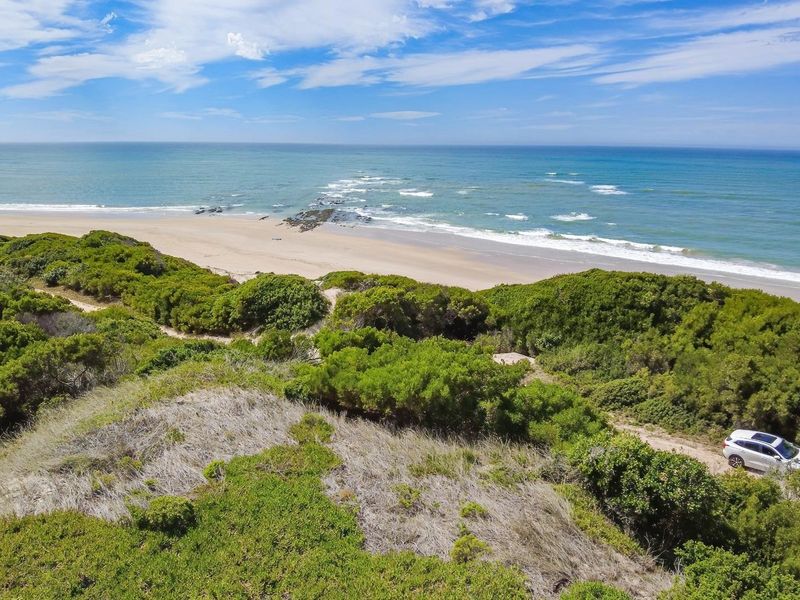 An elevated aerial view showcasing the pristine coastline, sandy beach, and natural coastal vegetation surrounding the property.
