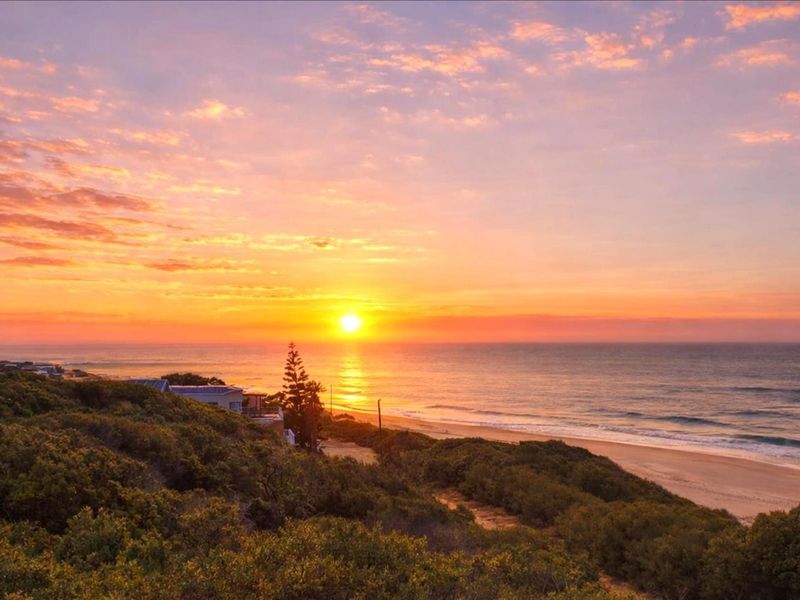 A stunning sunset view overlooking the coastline, featuring natural vegetation and direct beach access.