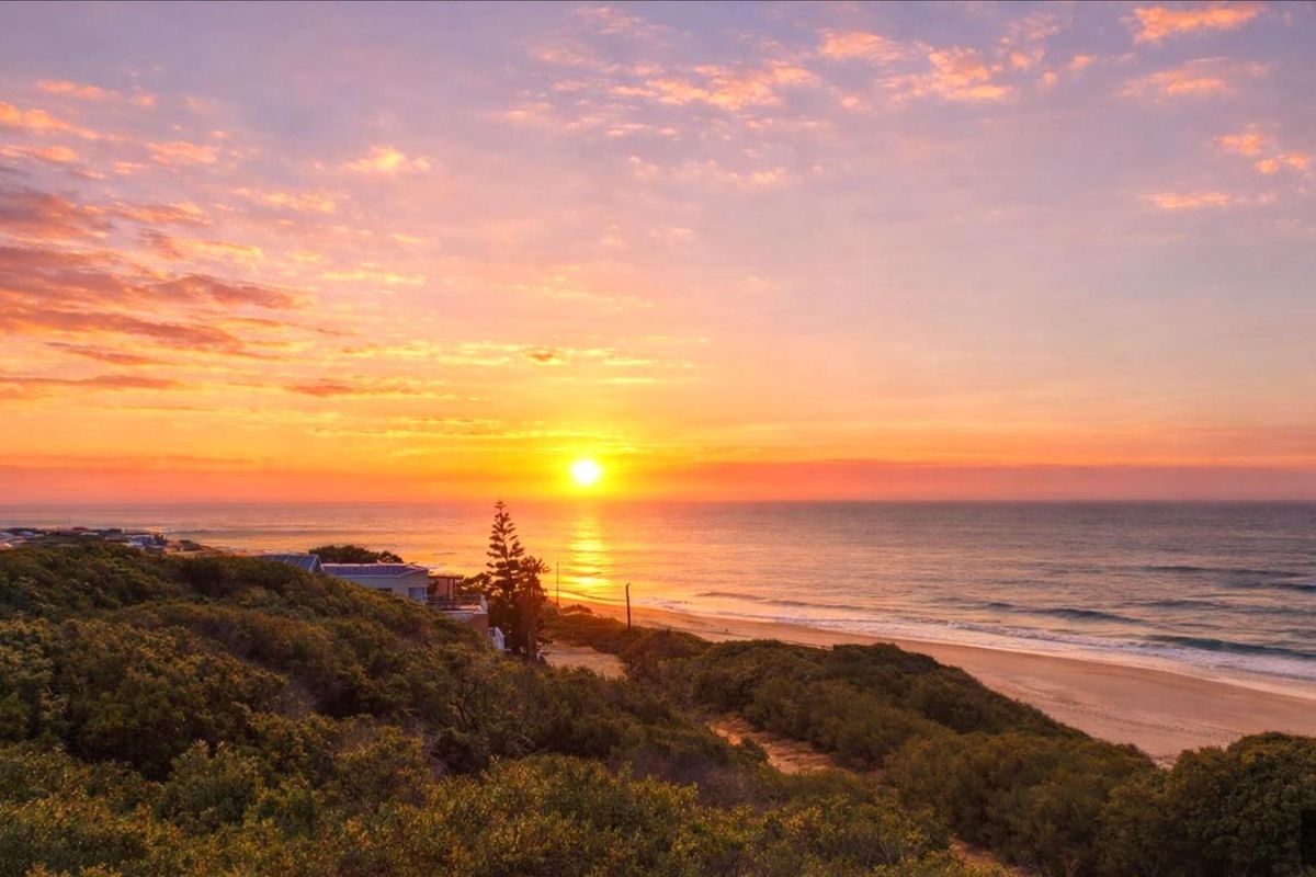 A stunning sunset view overlooking the coastline, featuring natural vegetation and direct beach access.