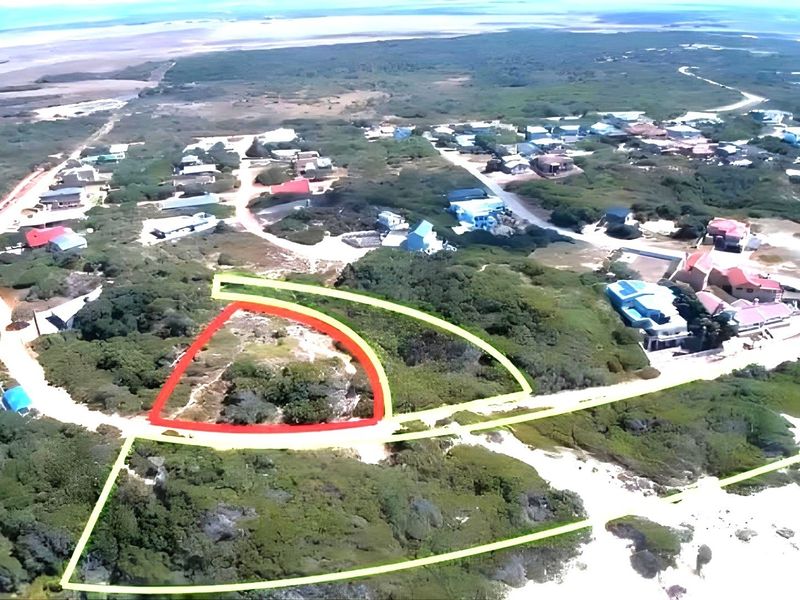 Aerial view of a vacant residential plot highlighted in red, situated within a coastal neighborhood with surrounding natural vegetation.