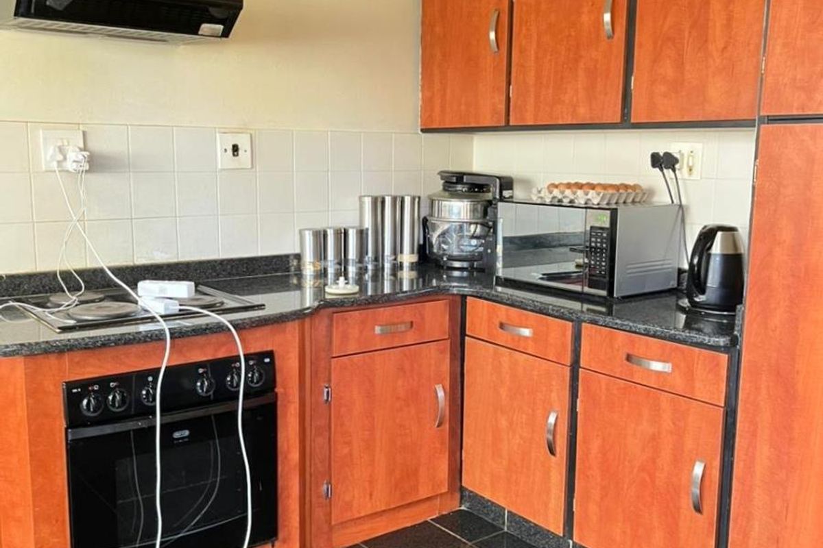 A functional kitchen featuring wood-tone cabinetry, dark granite countertops, a built-in oven, and a black extractor fan with a tiled backsplash.