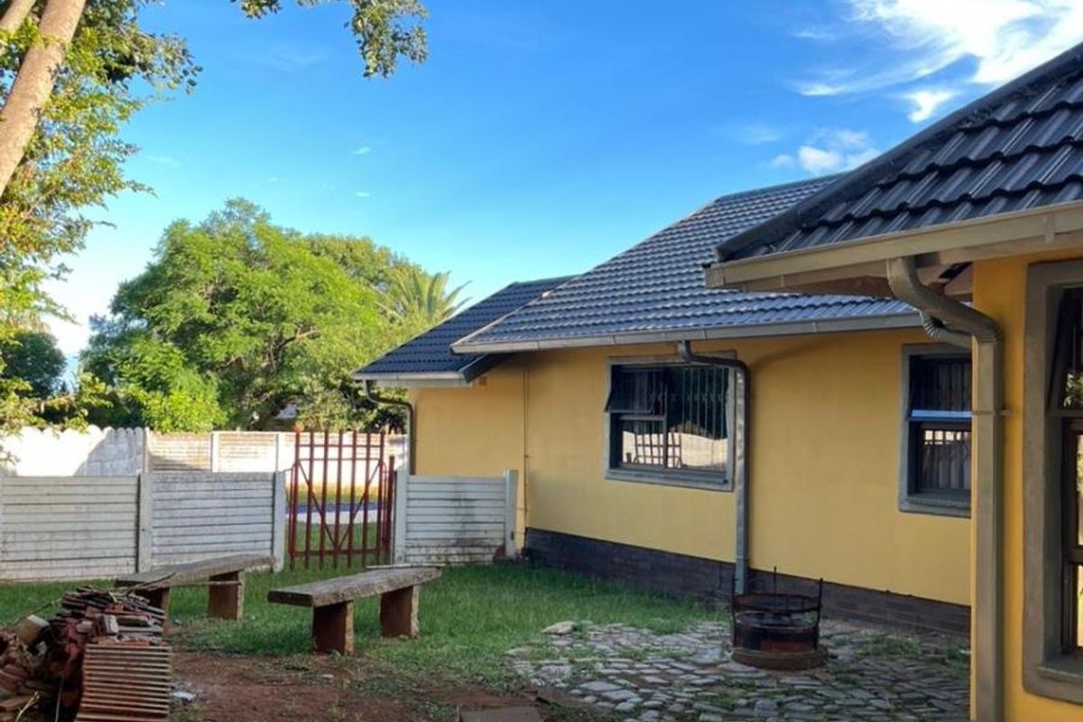 A rear exterior view of the house featuring a paved patio area, lawn, and perimeter fencing.