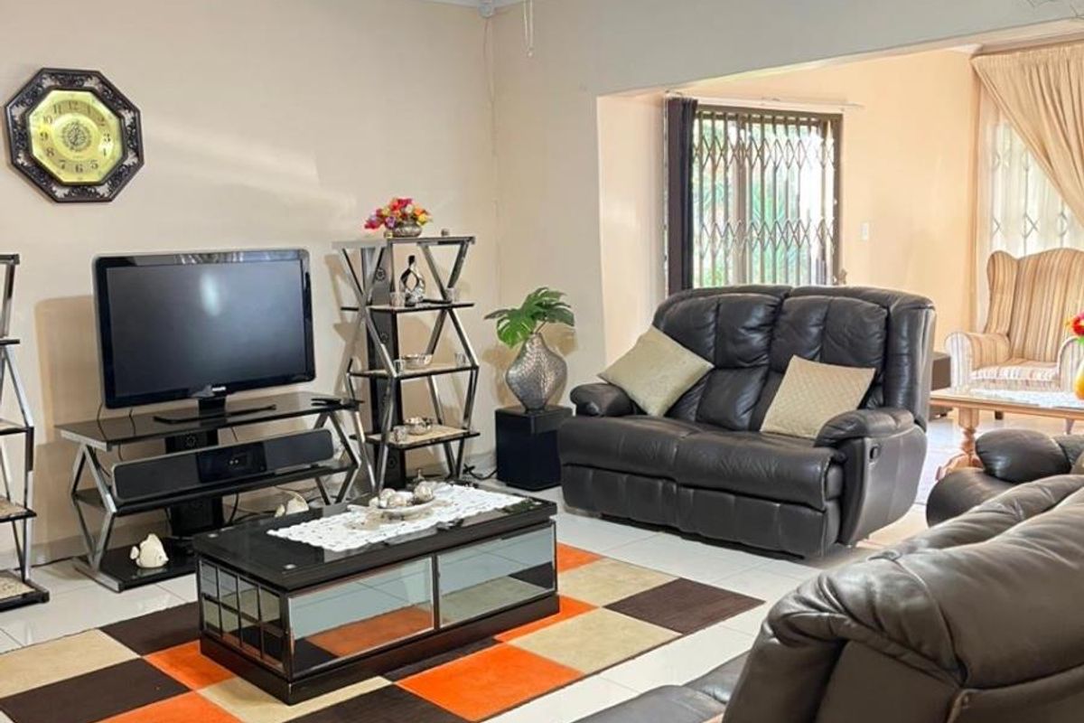A spacious living room featuring tiled flooring, a ceiling fan, and a large opening leading to an adjacent living area with security gates.