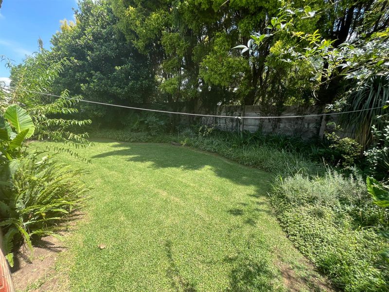 A private, well-maintained garden featuring a lush lawn, established perimeter landscaping, and a concrete boundary wall.