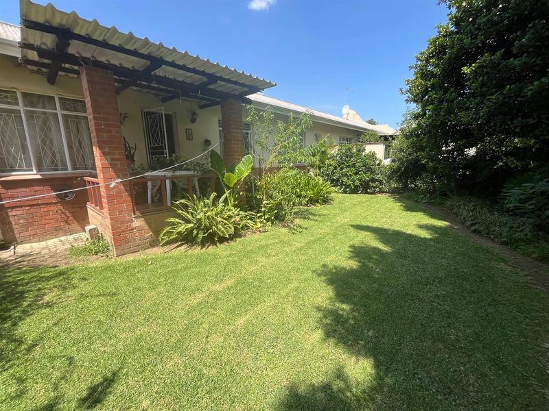 A view of the rear garden featuring a covered patio with brick pillars and a well-maintained lawn area.