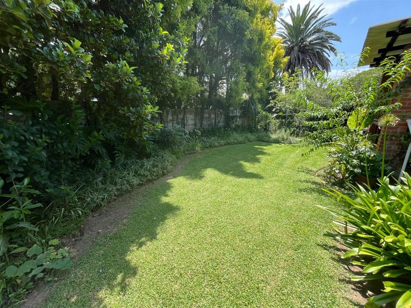 A private, established rear garden featuring a well-maintained lawn, mature trees, and perimeter boundary walling.