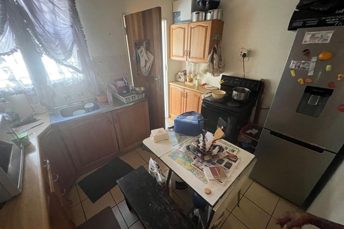 A compact kitchen featuring wooden cabinetry, a stainless steel sink, and tiled flooring, offering a functional layout with direct access to an exterior door.