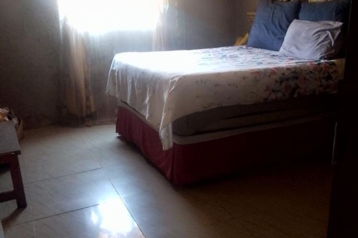 A bedroom featuring tiled flooring and natural light from a window, requiring cosmetic updates to wall finishes.