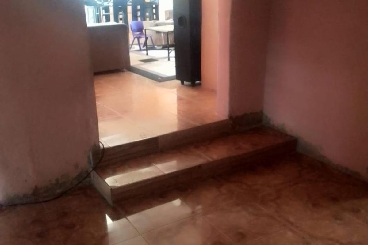 An interior view showing a split-level living area with tiled flooring and painted walls, connecting to an adjacent room.