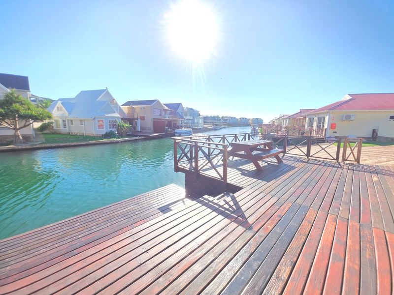 A waterfront timber deck overlooking a canal, featuring a built-in railing and direct access to the water in a residential estate setting.