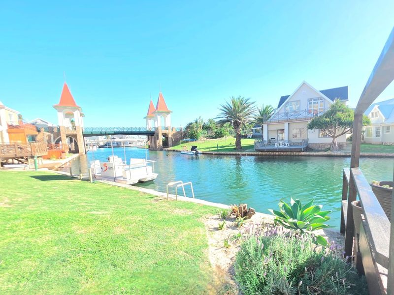 A scenic view of the canal-side property featuring landscaped gardens, a private jetty, and a bridge in the background.