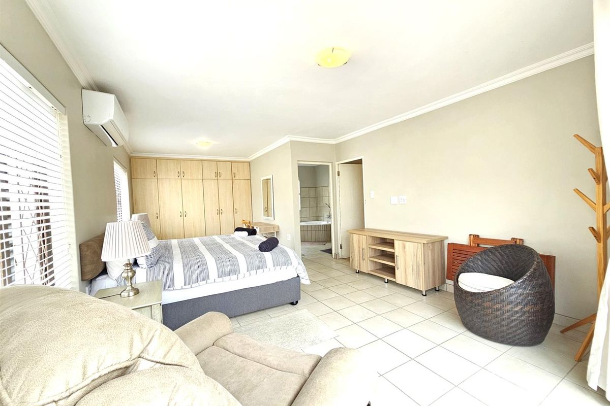 Spacious bedroom featuring built-in wooden cabinetry, tiled flooring, an en-suite bathroom access, and a wall-mounted air conditioning unit.