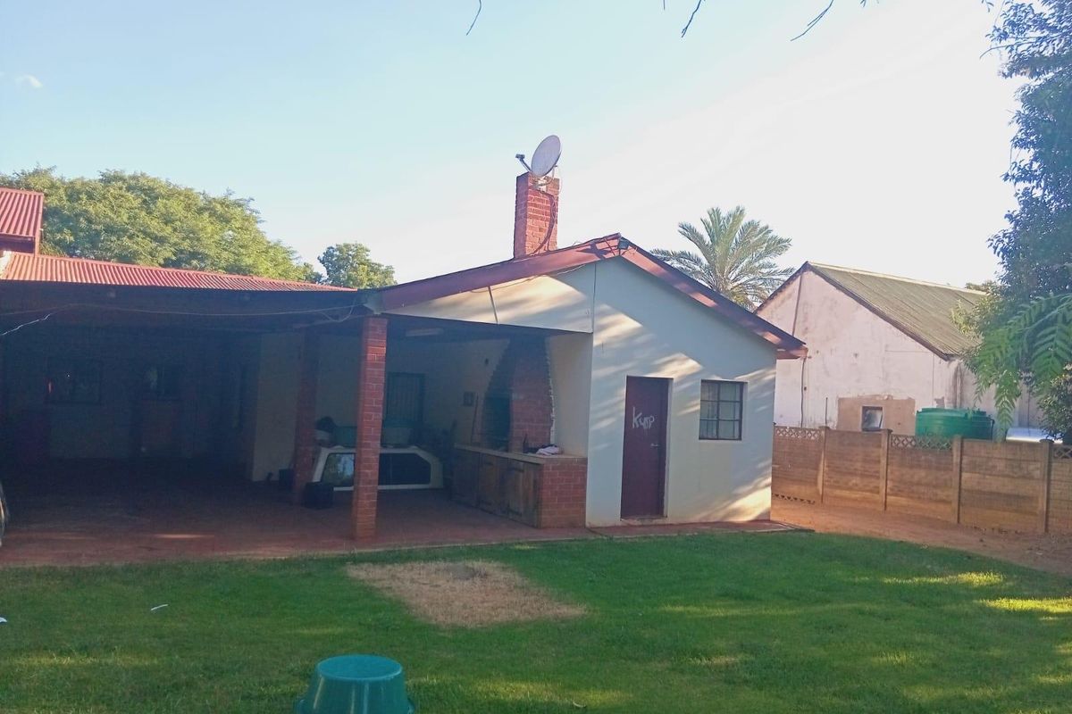 Rear view of the property featuring a covered patio area with a built-in braai, brick chimney, and a spacious garden.