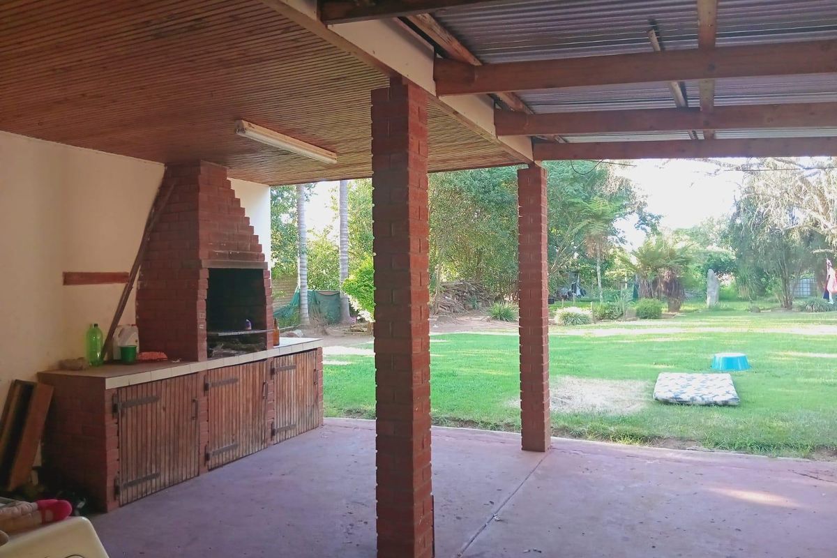 Covered outdoor patio featuring a built-in brick braai, timber ceiling, and exposed rafters, overlooking a spacious garden area.