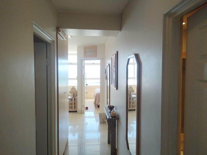 A bright hallway with tiled flooring leading towards a sunlit living area, providing access to multiple rooms within the apartment.