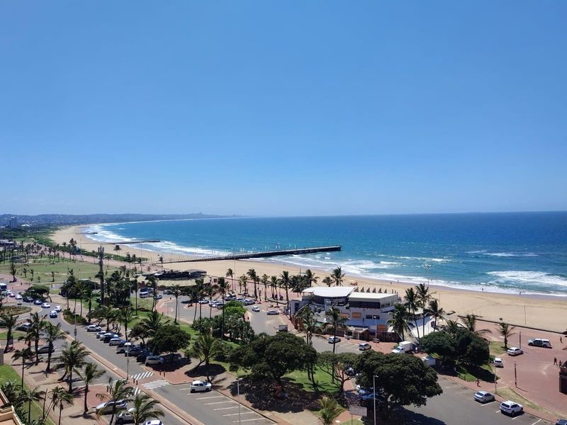 A panoramic elevated view overlooking the coastline, beach, pier, and surrounding urban landscape.