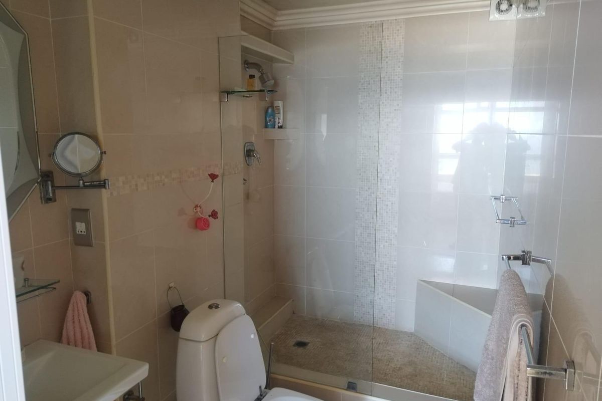 A compact bathroom featuring a walk-in shower with glass enclosure, wall-mounted toilet, and neutral tiled finishes.