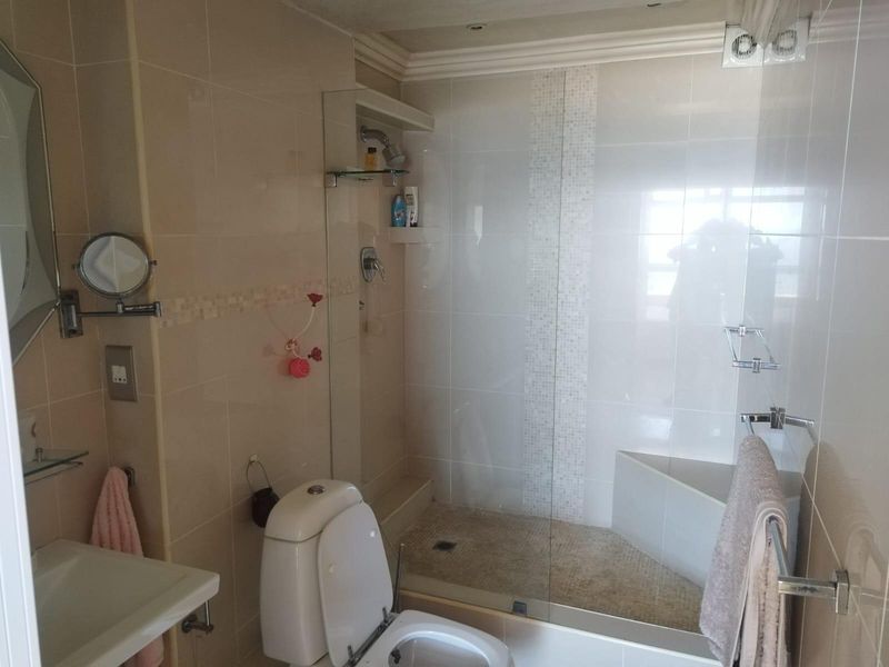 A compact bathroom featuring a walk-in shower with glass enclosure, wall-mounted toilet, and neutral tiled finishes.