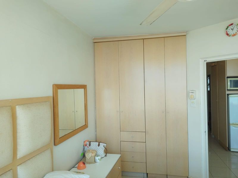 A bedroom featuring built-in light wood cabinetry with integrated drawers and a ceiling fan, providing functional storage and climate control.