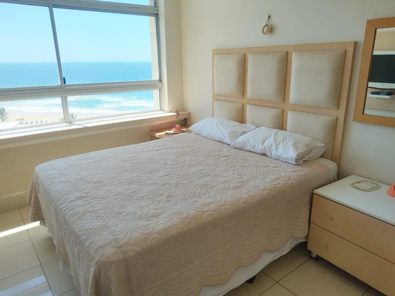 A bedroom featuring large windows with direct ocean views, tiled flooring, and a neutral color palette.
