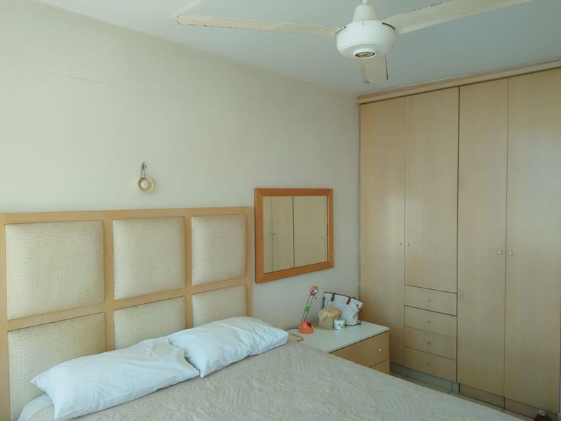 A bedroom featuring built-in wooden cabinetry, a neutral upholstered headboard, and a ceiling fan, offering a functional and well-organized living space.