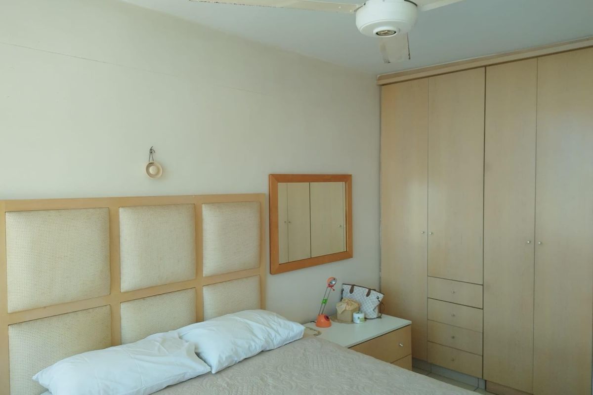 A bedroom featuring built-in wooden cabinetry, a neutral upholstered headboard, and a ceiling fan, offering a functional and well-organized living space.