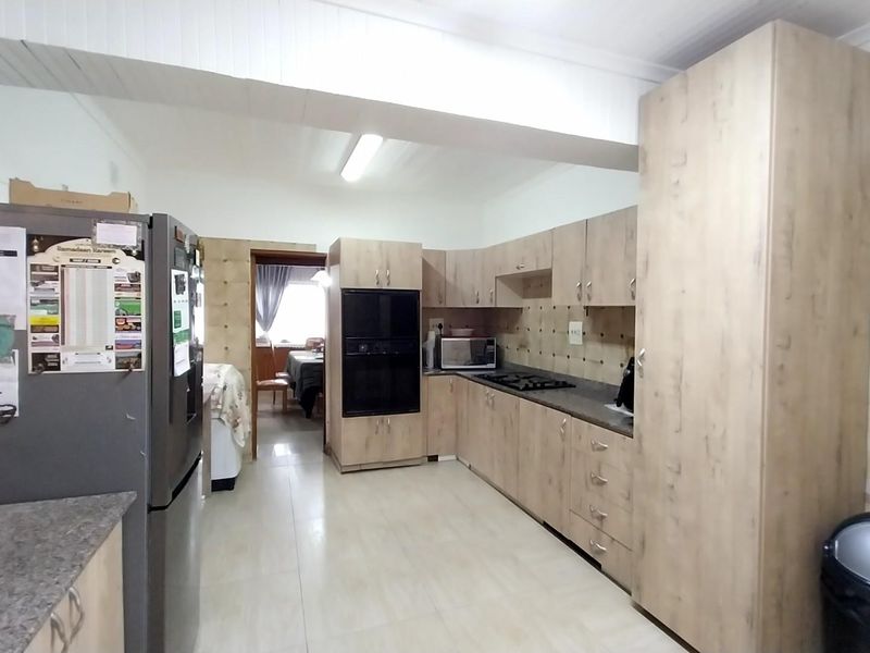 A functional kitchen featuring light wood-tone cabinetry, built-in oven, gas hob, and tiled splashbacks with neutral floor tiles.