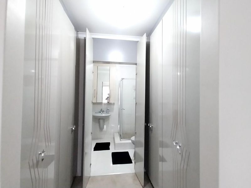 A clean bathroom featuring built-in storage cupboards in the hallway leading to a pedestal basin, shower enclosure, and toilet.